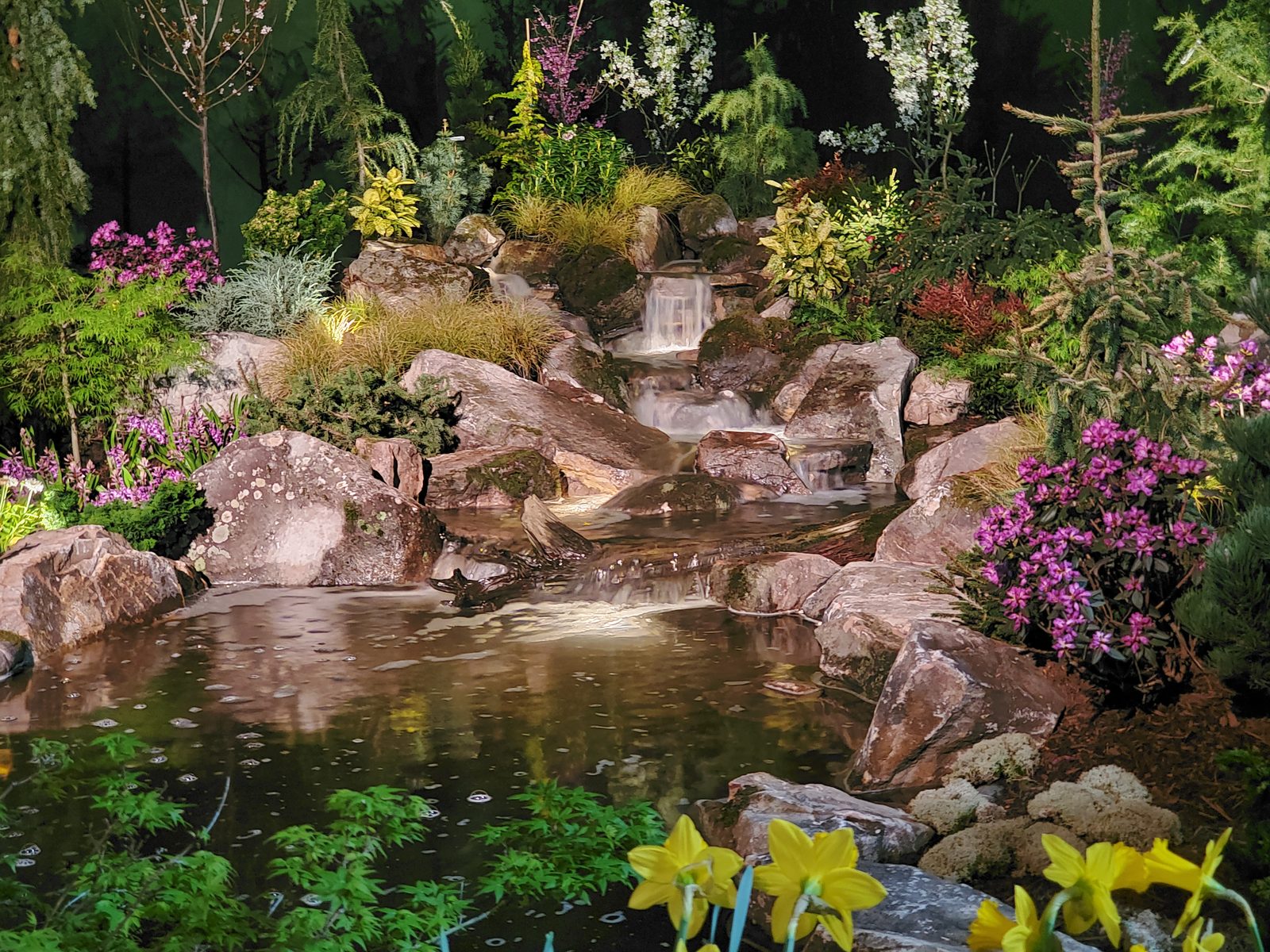 A multi-tier boulder waterfall and pond surrounded by azaleas, daffodils, and Japanese maples, built as a temporary show garden